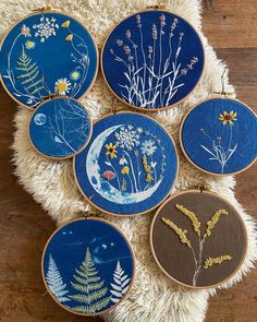 six embroidery hoops with flowers and plants on them sitting on a white furnishing