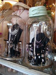 two glass jars with necklaces and other items in them sitting on a shelf next to each other