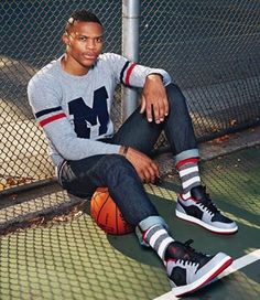 a young man sitting on the ground next to a fence