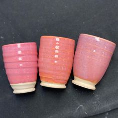 three pink cups sitting next to each other on a black tableclothed surface,