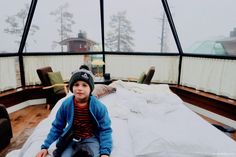 a young boy sitting on top of a bed in a room filled with furniture and windows