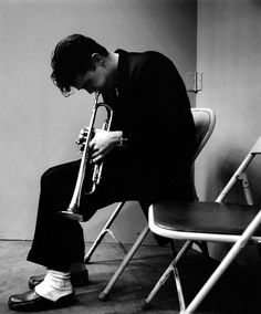 black and white photograph of a man playing a trumpet in a room with chairs around him