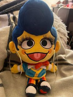 a small stuffed toy with big eyes and blue hair sitting on top of a bed