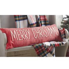 a red christmas pillow sitting on top of a white bench next to a tree and plaid blanket