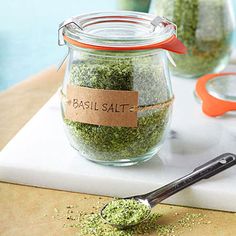 a glass jar filled with basil salt next to a measuring spoon