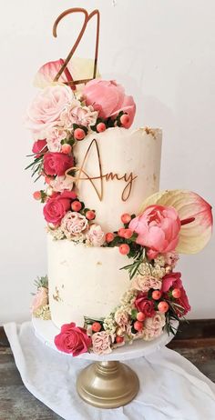 a three tiered cake with pink flowers and greenery on the top is displayed