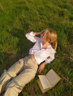 a woman laying in the grass reading a book