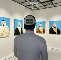 a man wearing a hat standing in front of paintings