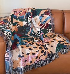 a couch with a blanket on top of it next to a brown leather chair in front of a white wall