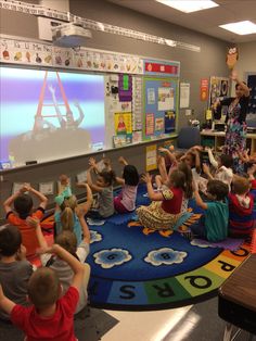 a group of children sitting on the floor in front of a projector screen and teacher