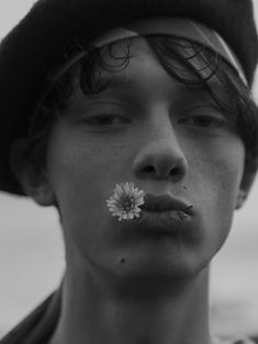 a young man with a flower in his mouth is wearing a hat and nose ring