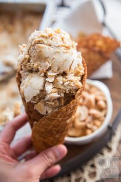 a person holding an ice cream cone filled with toppings on top of a table