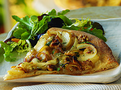 a slice of pizza on a white plate with greens and salad in the background at a restaurant