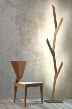 a wooden chair sitting next to a tree with no leaves on it in front of a concrete wall