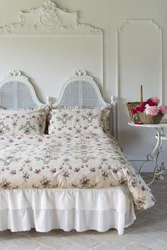 a white bed sitting next to a table with flowers on it and a basket full of pink roses