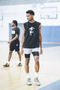 two men standing on a basketball court in shorts and t - shirts, one with a man's face on it