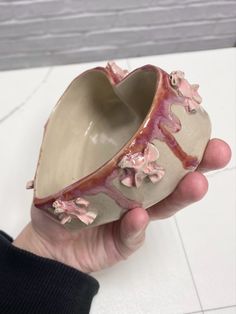 a hand holding a ceramic vase with pink flowers on it's side and inside