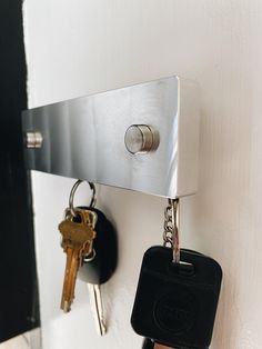 two keys are hanging on the wall and one is attached to a key holder with a metal hook