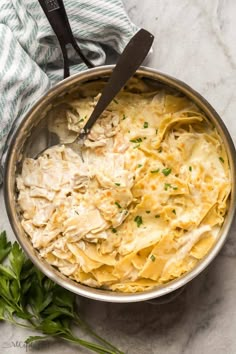 a pot filled with pasta and parsley on top of a marble counter next to a knife