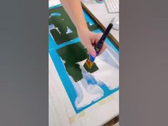 a person is using a brush to paint on a piece of paper with blue and green squares