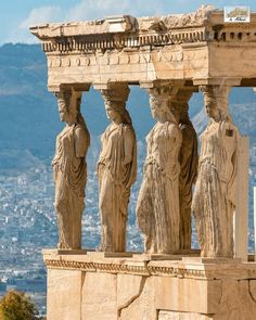 some statues on the side of a building with a city in the backgroud