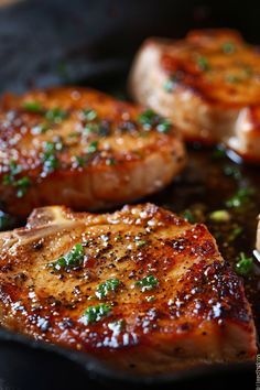 three pieces of meat are cooking in a frying pan on the stove with herbs and seasonings