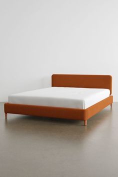 a bed with an orange headboard and foot board on it's side, against a white wall