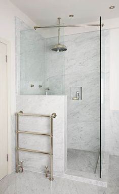 a bathroom with a glass shower door and white marble walls, along with a gold towel rack