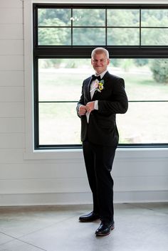 a man in a tuxedo standing next to a window