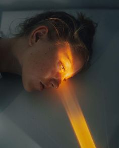 a woman is laying down with her head on the table and light coming from behind her