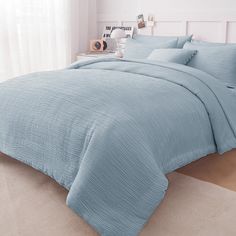 a bed with blue comforters and pillows in a white room next to a window