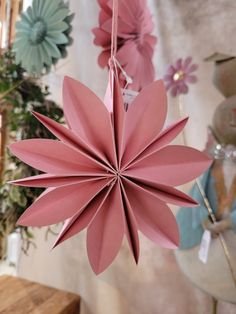 a pink origami flower hanging from a string in front of some other flowers