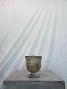 an old bowl sitting on top of a cement block in front of a white backdrop