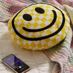 a smiley face pillow sitting on top of a bed next to a cell phone