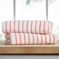 two orange and white striped towels sitting on top of a wooden table next to a window