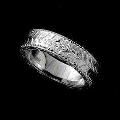 a wedding ring with leaves engraved on the side in white gold, against a black background