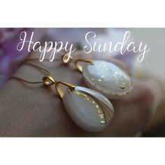 a woman's hand holding two white and gold earrings with the words happy sunday written on it