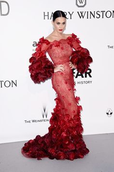 a woman in a long red dress standing on a white carpet with her hand on her hip