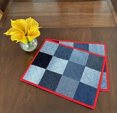 a vase with yellow flowers sitting on top of a wooden table next to two quilted placemats