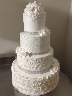 a three tiered wedding cake with white flowers on top and silver ribbon around the edges