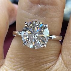 a woman's hand holding a diamond ring on her finger, with the center stone in