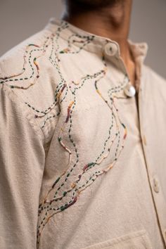 a close up of a man wearing a white shirt with colorful stitching on it