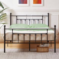 a black metal bed frame with green sheets and pillows in a white room next to a potted plant