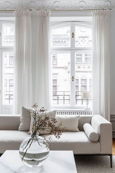 a living room filled with white furniture and large windows covered in sheer curtained drapes