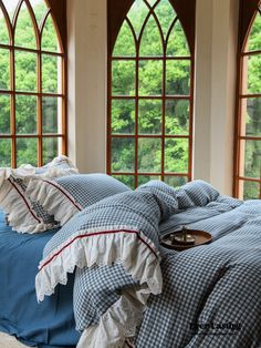 a bed with blue sheets and pillows in front of two large arched windows that look out onto the woods