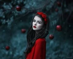 a woman with long black hair and red lipstick is standing in front of an apple tree