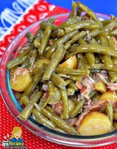 green beans and potatoes in a glass bowl on a red tablecloth with a spoon