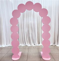 a pink arch with circles on it in front of a white curtain and tile floor