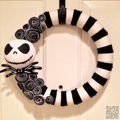 a wreath with a skeleton on it hanging from the side of a door, decorated with black and white yarn