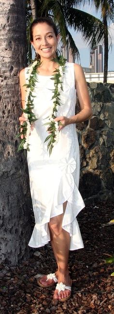 a woman standing next to a palm tree wearing a white dress with green leaves on it